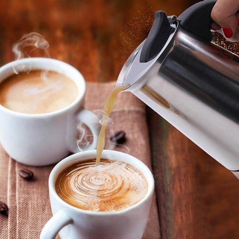Pouring freshly brewed coffee from a stainless steel moka coffee maker into white cups.