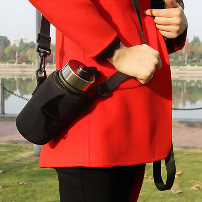Person holding a sports water bottle carrier bag while wearing a red coat outdoors.