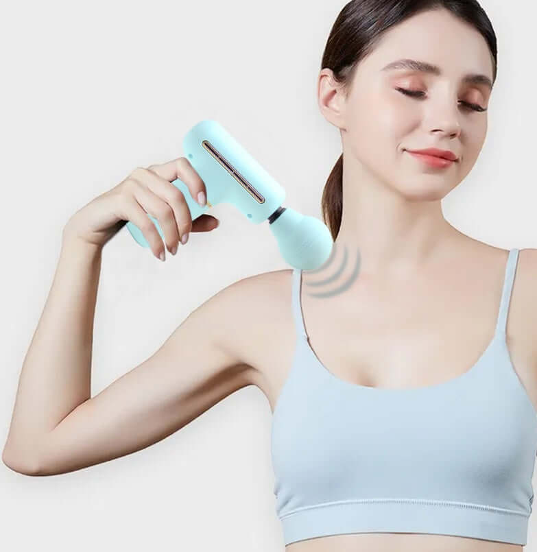 Woman using a portable muscle massage gun on her shoulder to relax muscles after a workout.