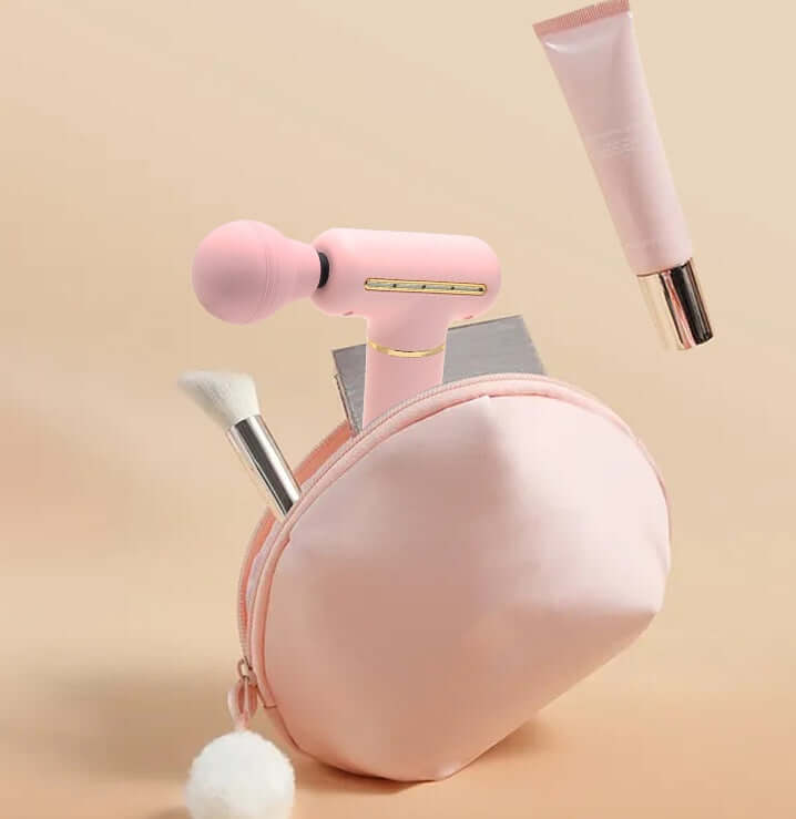 Portable muscle massage gun in pink bag with cosmetic items for relaxation and beauty routine.