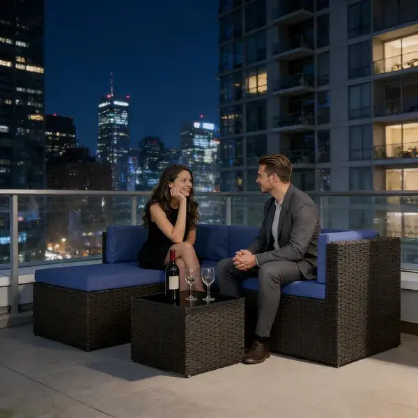 Couple enjoying drinks on outdoor patio furniture set with city skyline at night.